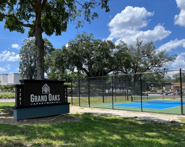 Grand Oaks Apartments entrance sign beneath mature oaks
